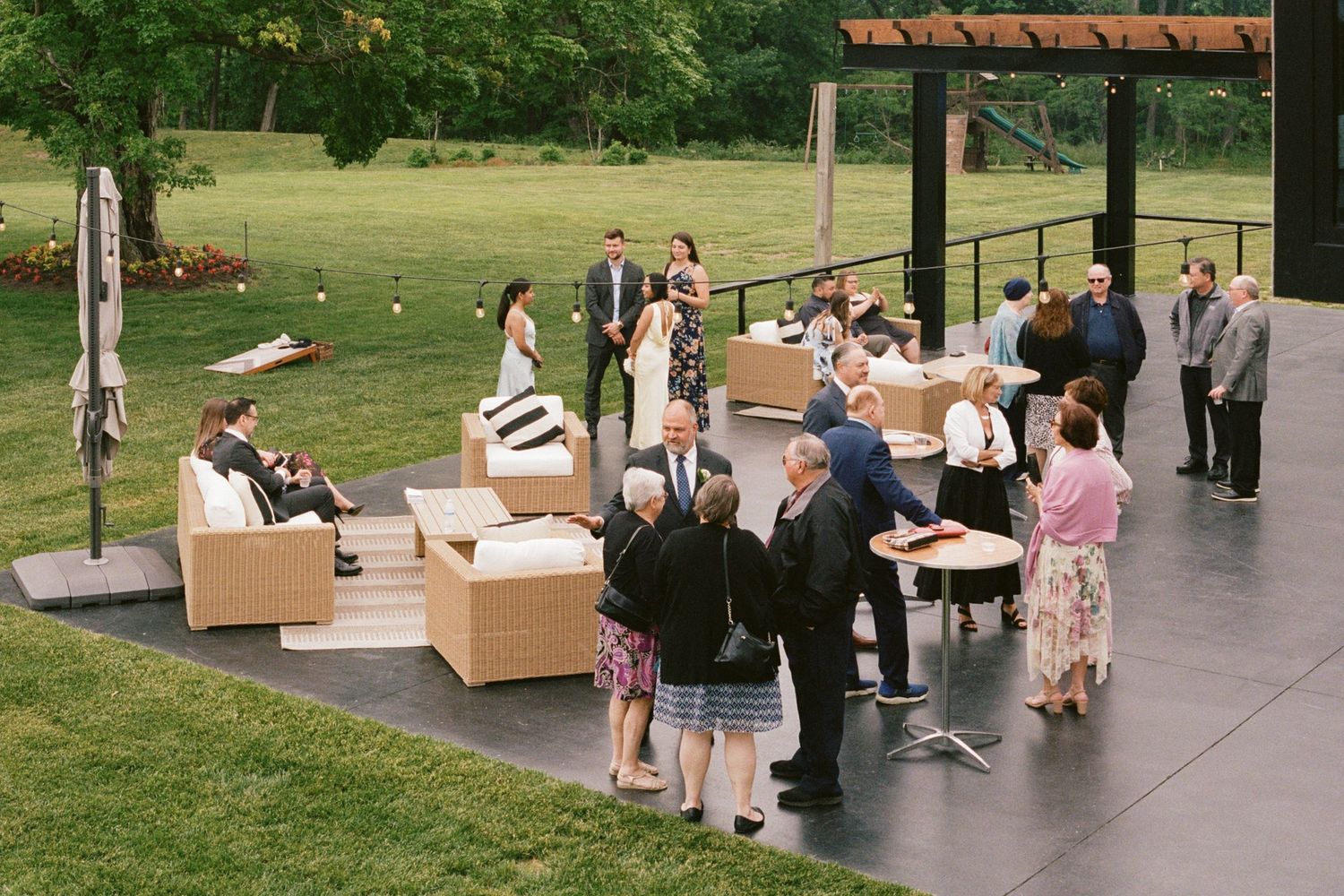 Guests mingle outdoors on a modern patio with wicker furniture during an elegant garden wedding reception.