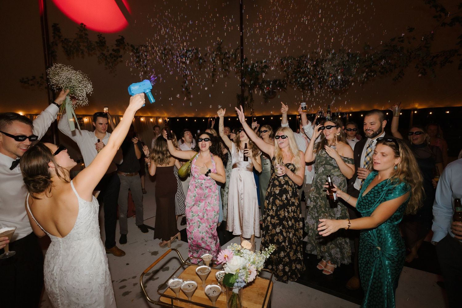 Excited wedding guests raise hands as confetti fills the air during a lively wedding reception celebration.