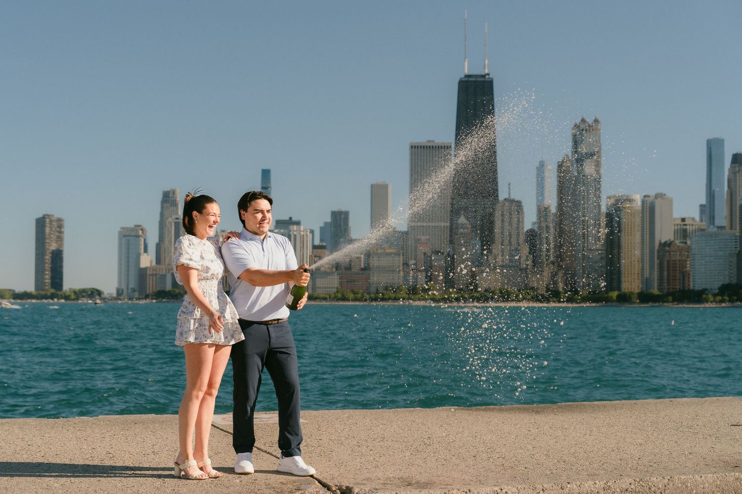 Engaged couple celebrating with champagne spray by Lake Michigan and Chicago skyline.