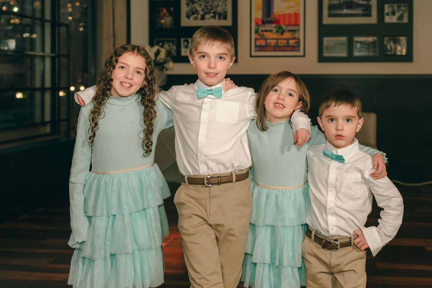 Four children in matching mint green and white wedding attire pose together smiling.