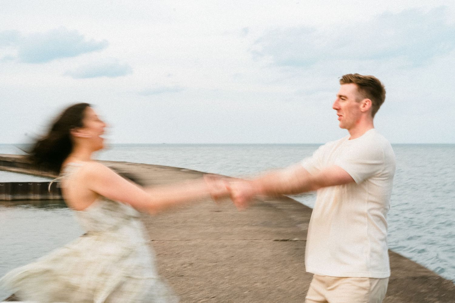 Couple joyfully spinning on a pier by the ocean, motion blur capturing their playful energy.