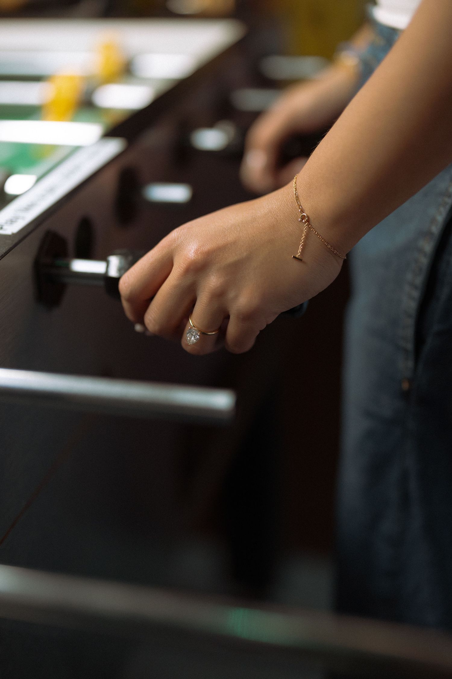 Close-up of a woman's hand with a ring and gold bracelet gripping a foosball table handle.