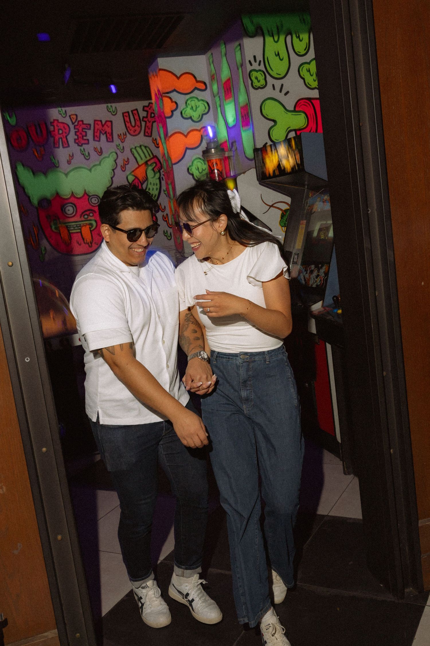 Happy couple walking hand in hand through a doorway in a vibrant arcade venue.