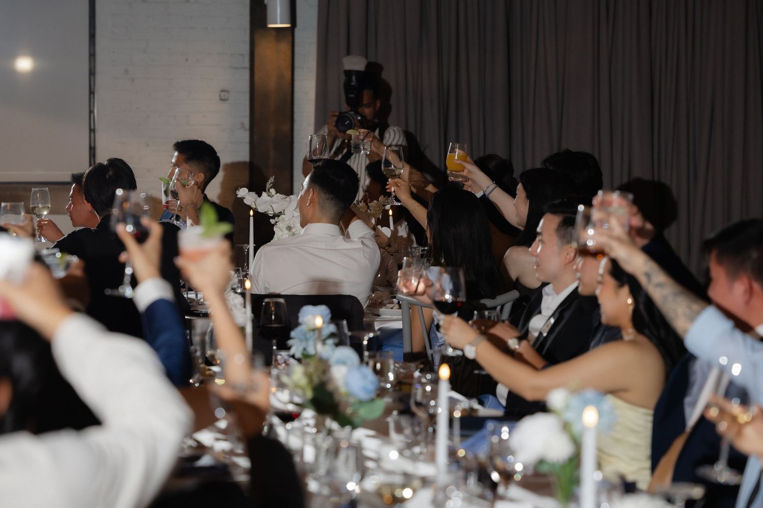 Wedding guests raise glasses in a toast at elegant reception dinner.