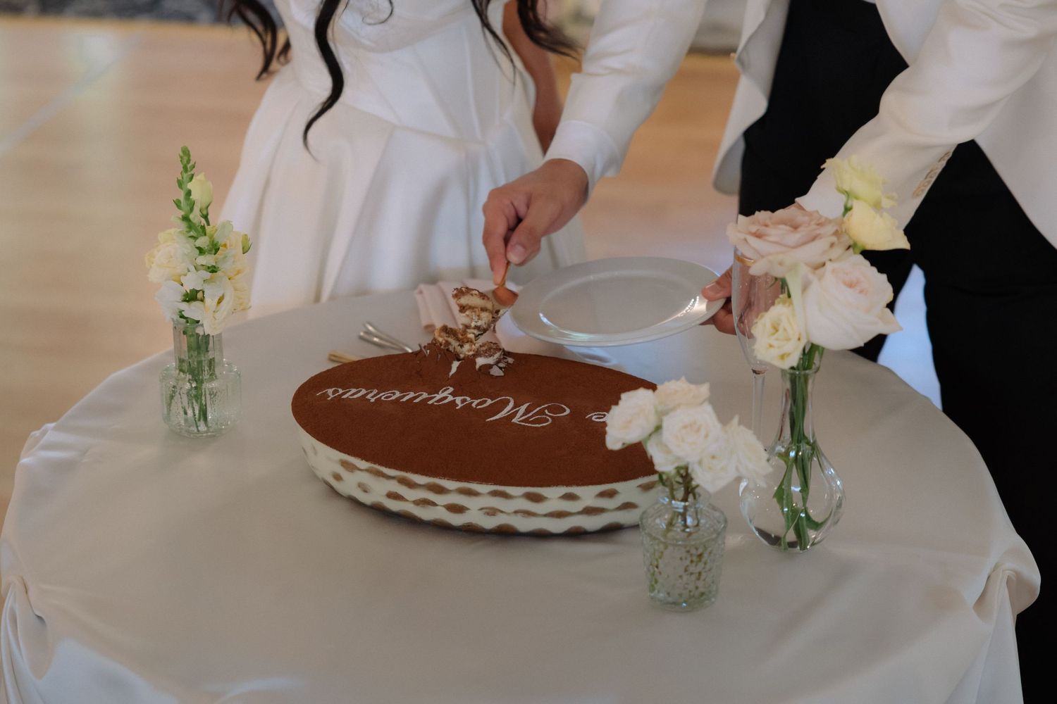 Bride and groom cutting their tiramisu wedding cake surrounded by delicate floral arrangements.