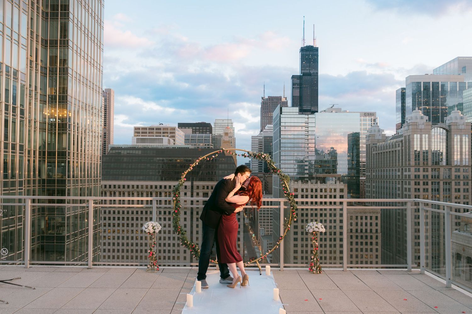 Engaged couple embraces on white aisle runner on Chicago rooftop at golden hour with skyline views.