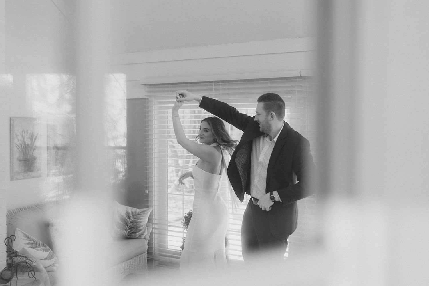 Black and white photo of newlyweds sharing a dance together in a sunlit room after wedding.