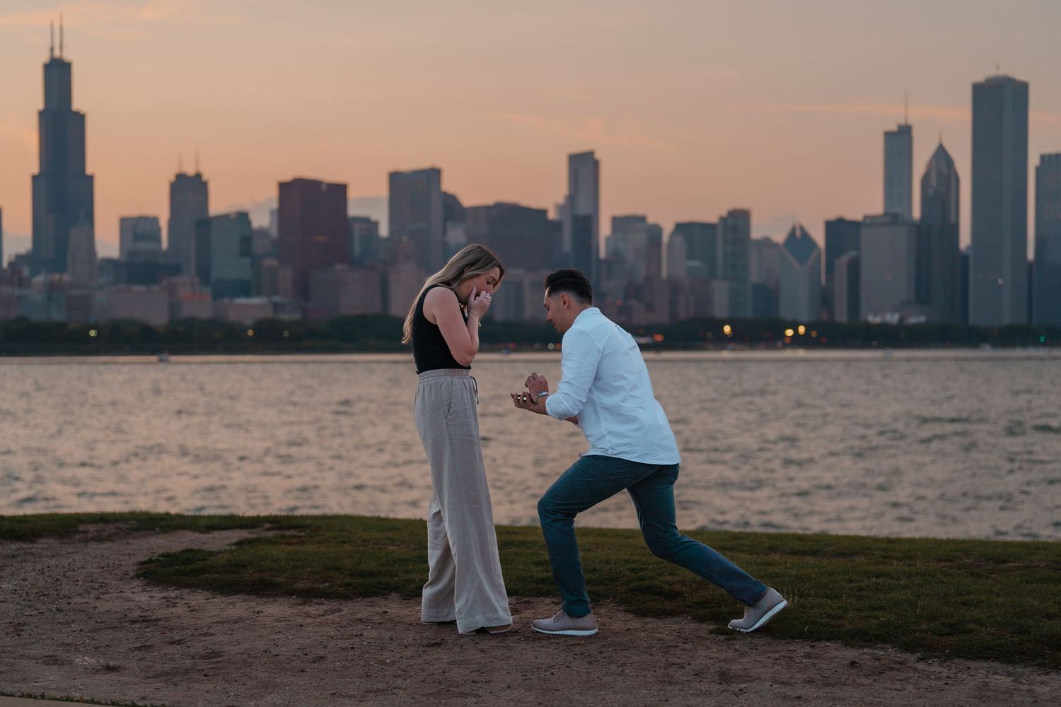 Man getting down on one knee to propose to woman near Chicago lakefront at sunset.