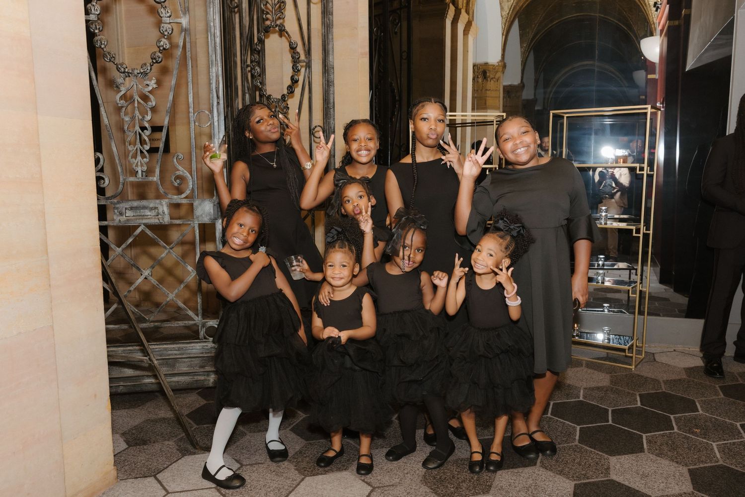 Group of young girls and a woman posing together in matching black dresses at a formal event.