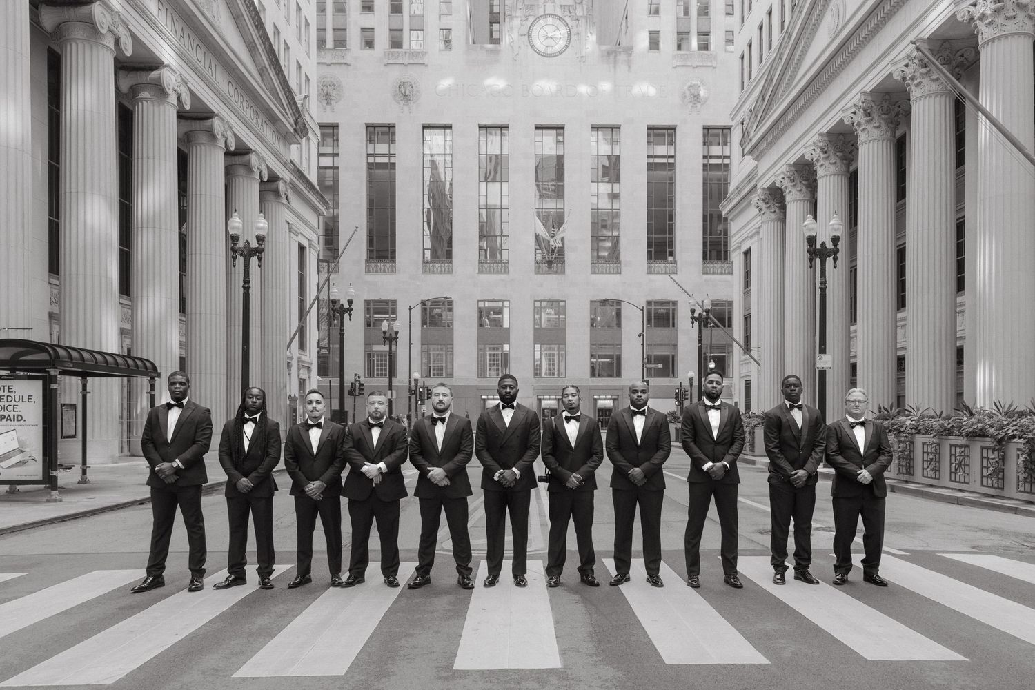Black and white photo of groomsmen in tuxedos lined up in a grand columned building hall.