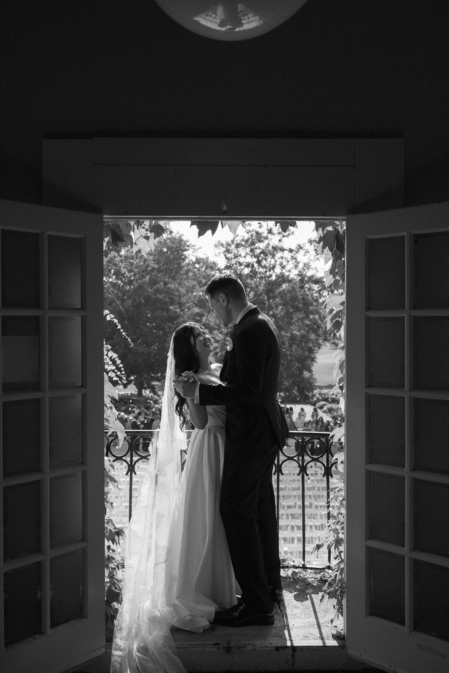 Black and white silhouette of bride and groom embracing in doorway with garden backdrop.