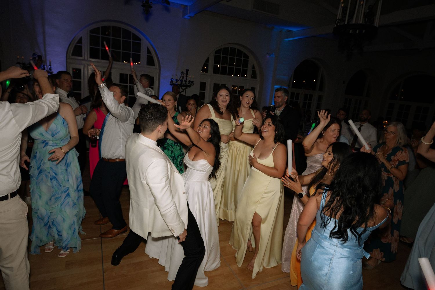 Guests dancing energetically at a wedding reception in an elegant ballroom with blue lighting.