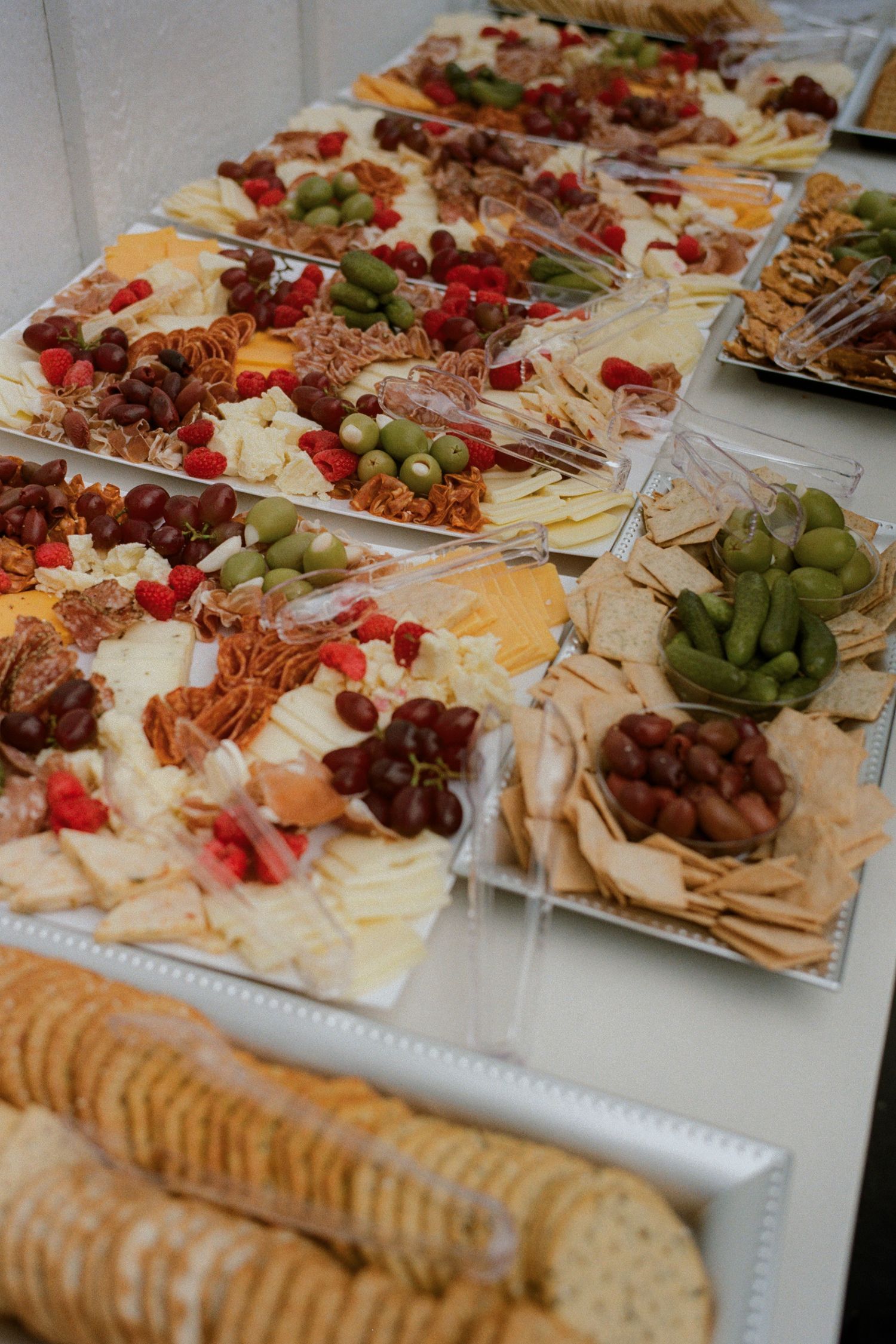 Elegant charcuterie boards with cheese, crackers, grapes, and cured meats arranged on a white table for a catered event.