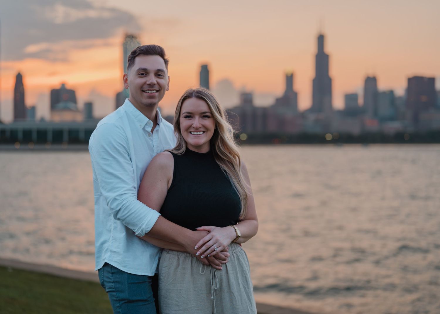 Happy couple posing together with the Chicago skyline glowing orange at sunset behind them.