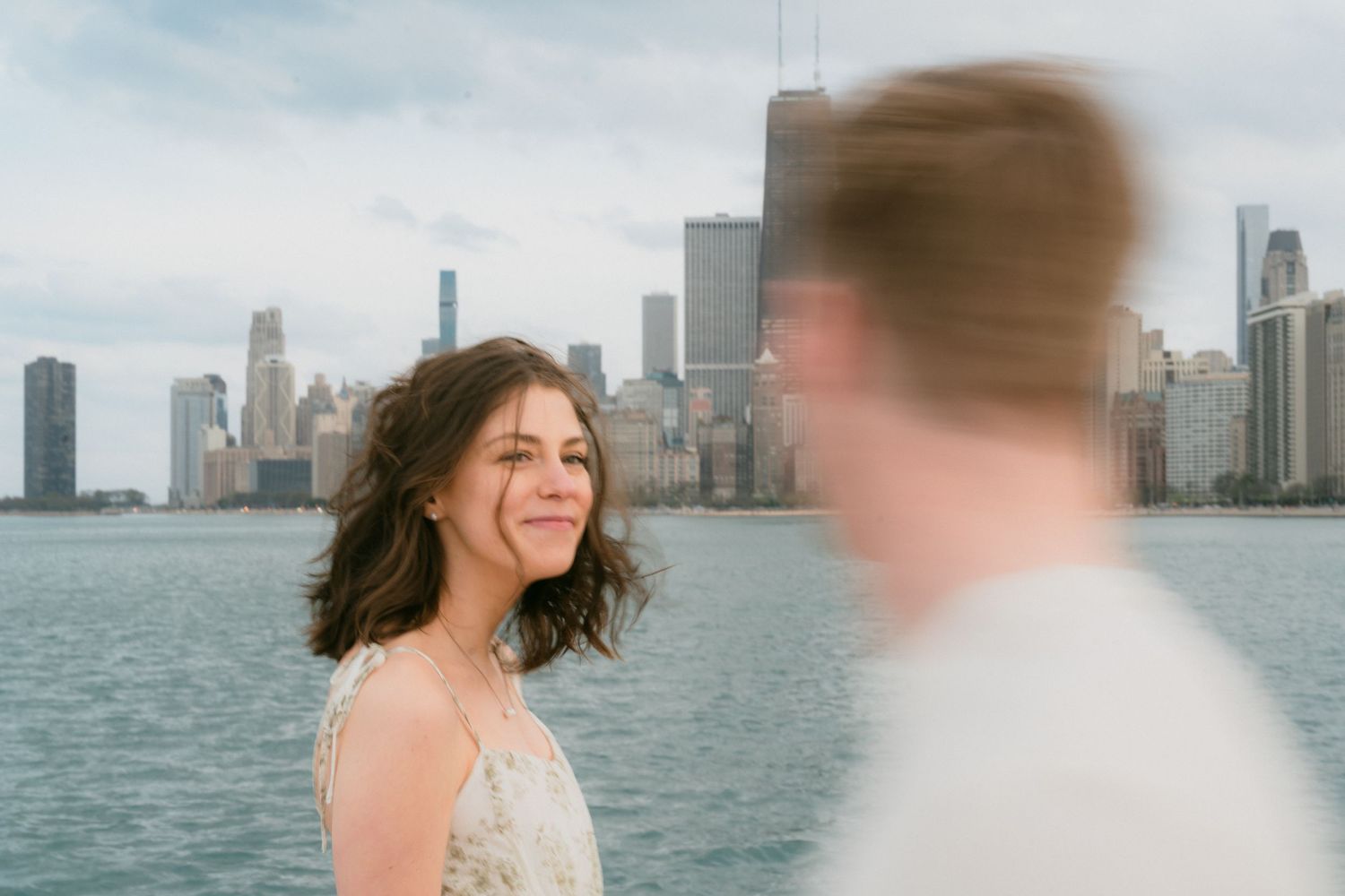 Woman smiling softly with Chicago skyline and lake visible in background.