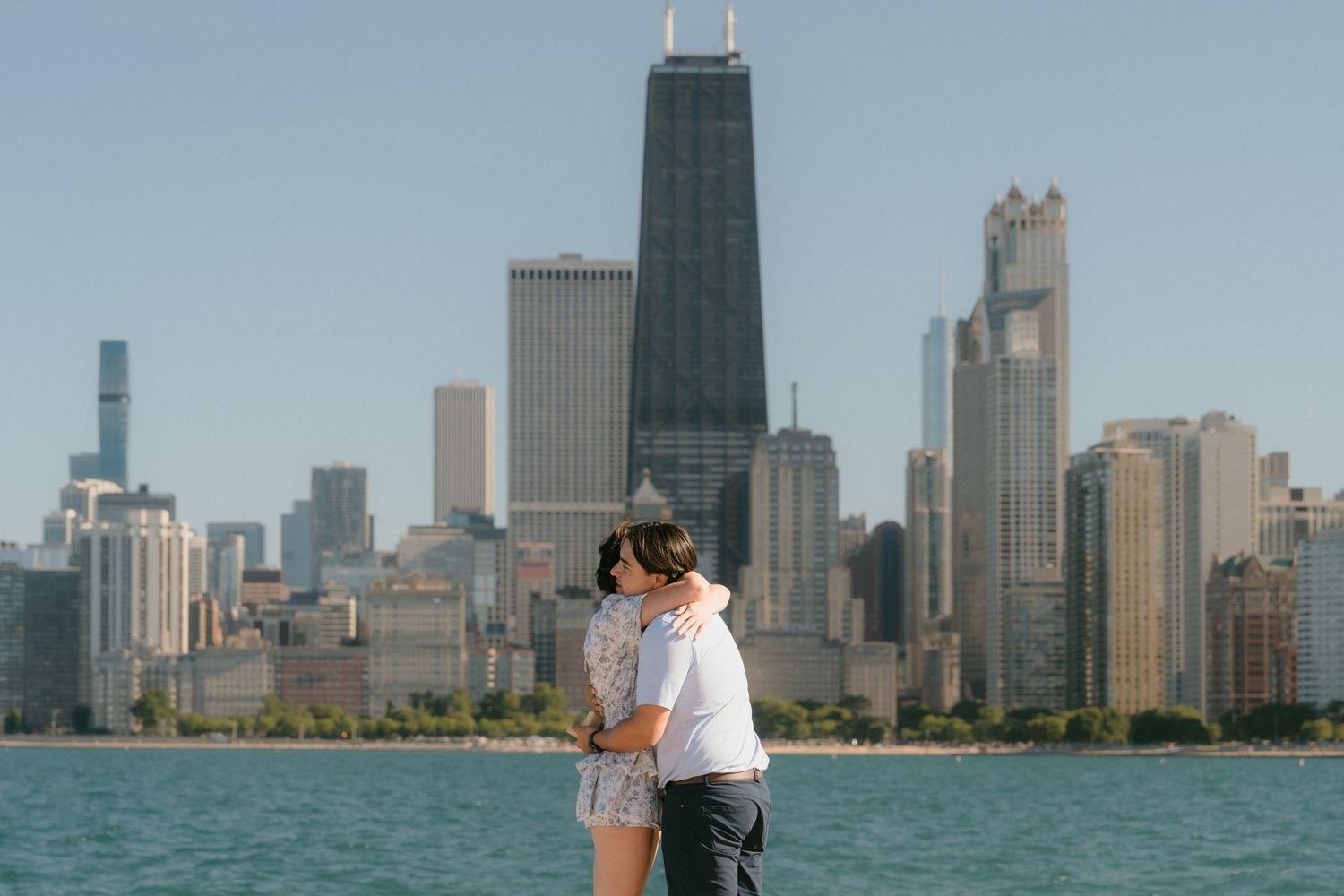 Newly engaged couple kissing with stunning Chicago skyline in background.