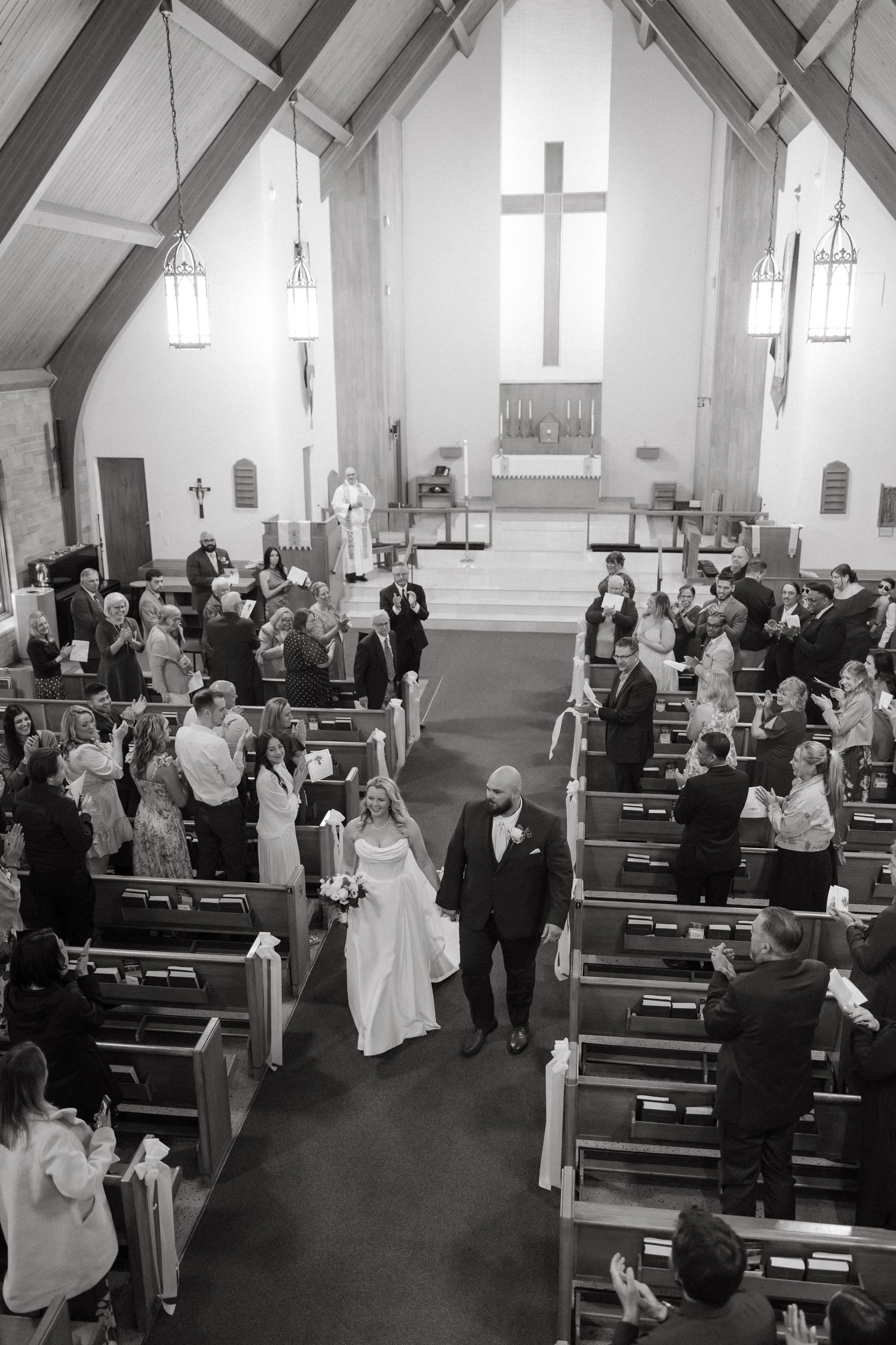 Black and white photo of a bride and groom walking down the church aisle after their wedding ceremony.