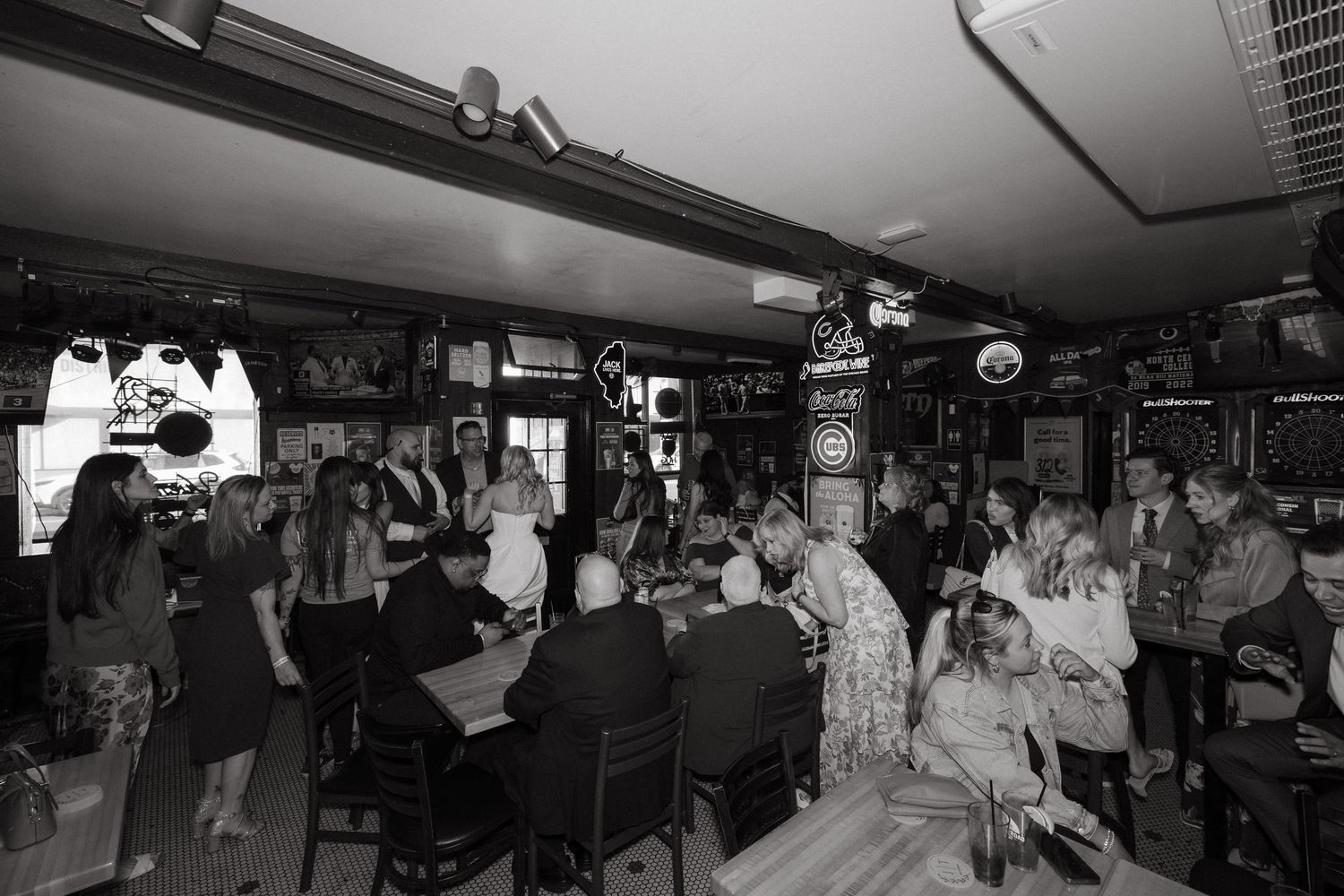 Black and white photo of a lively crowded bar with patrons socializing at tables and along the counter.
