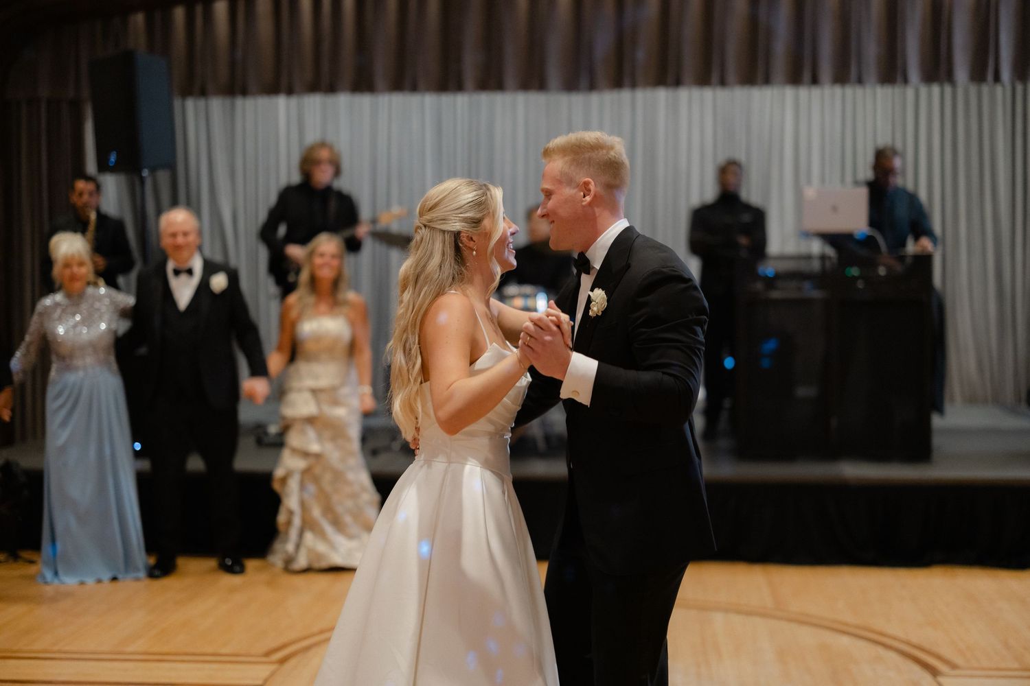 Bride and groom share first dance at elegant wedding reception with live band performing in background.