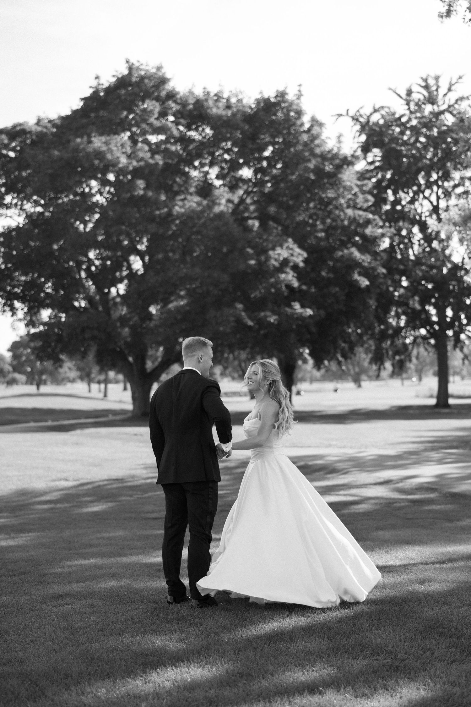 Bride and groom walk hand in hand across a golf course in a romantic black and white photo.