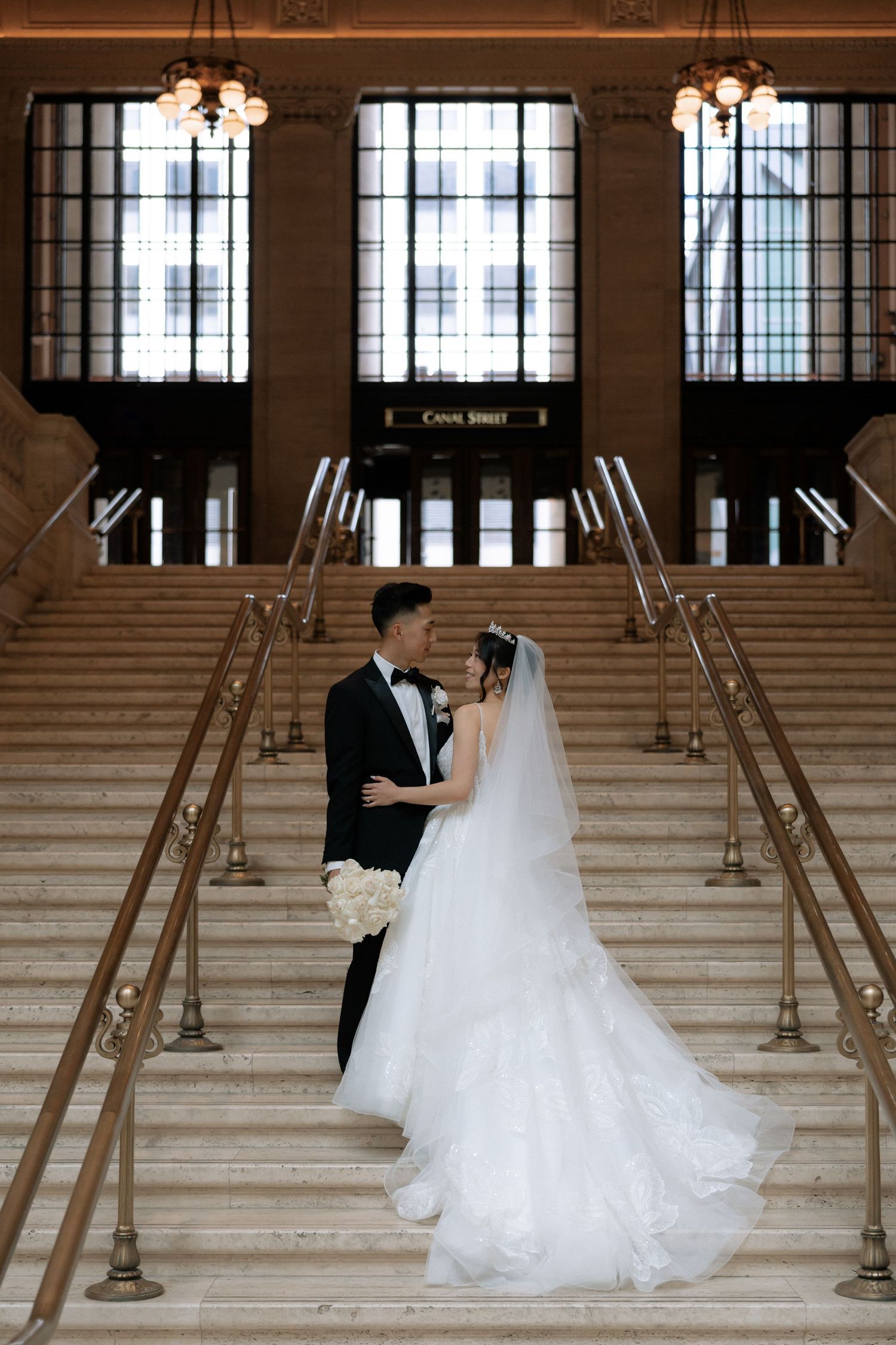 Bride and groom share romantic moment on grand staircase in elegant historic building during wedding portraits.