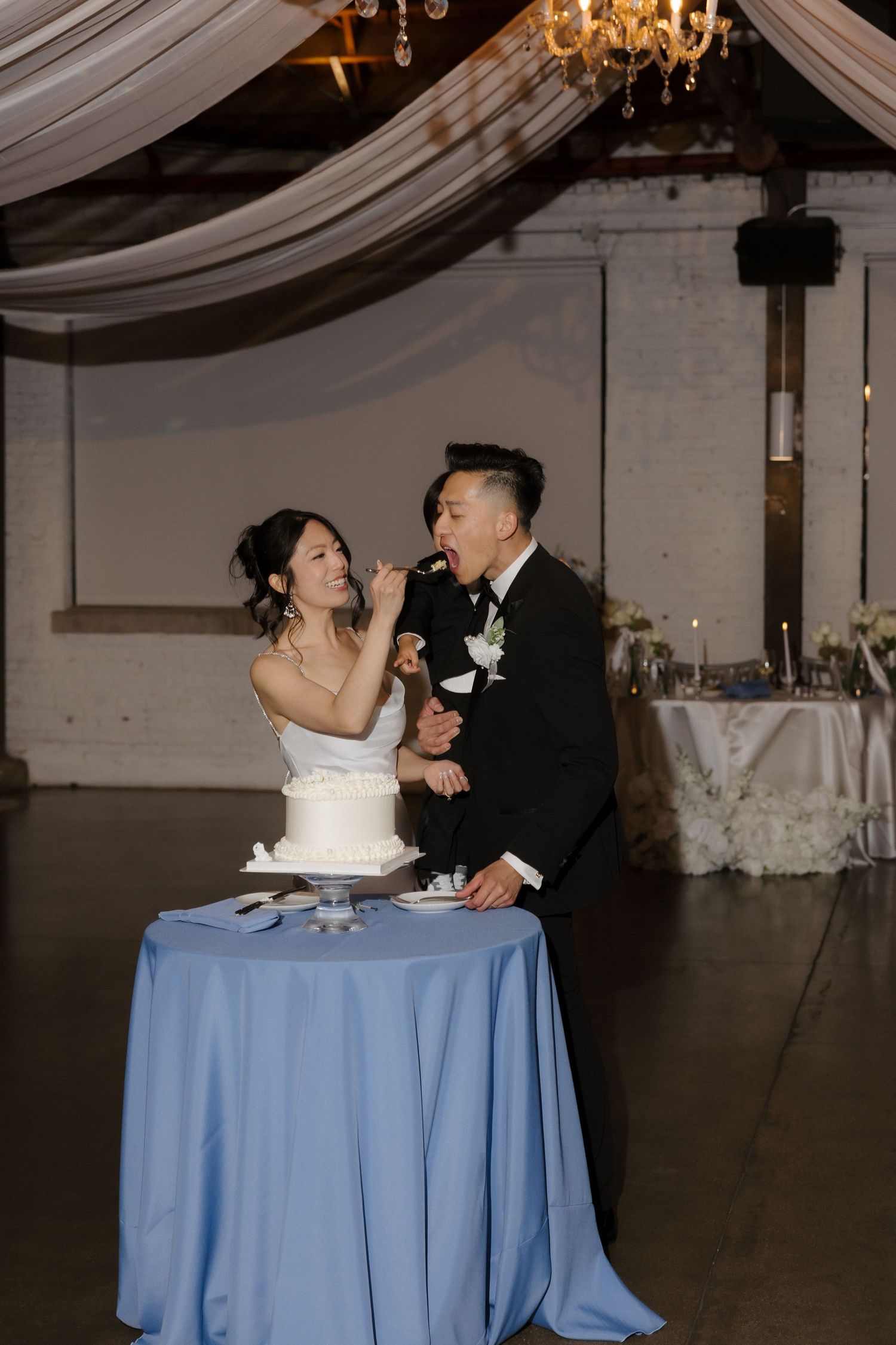 Bride and groom sharing cake at their wedding reception in an elegant industrial venue.