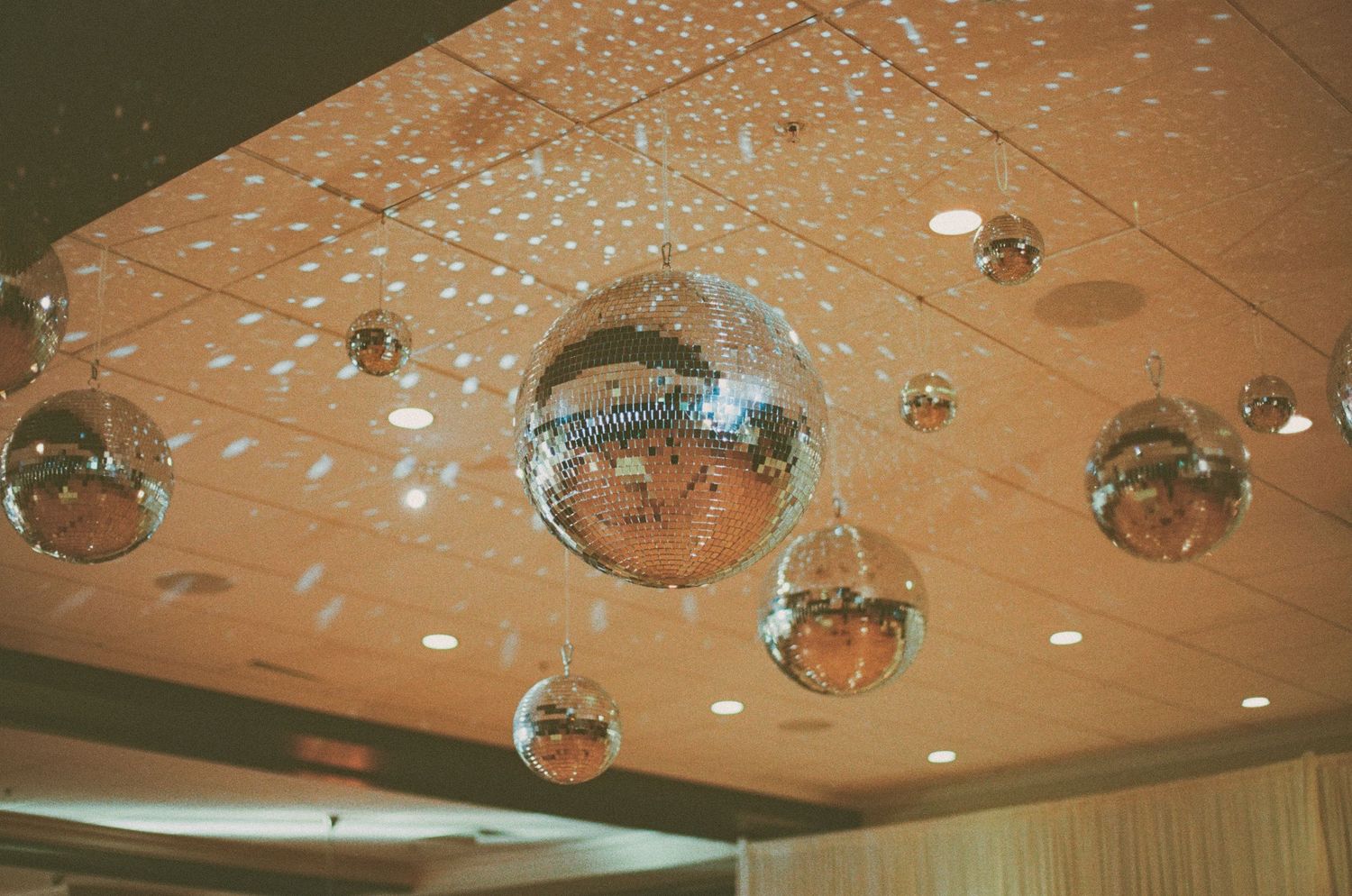 Sparkling disco mirror balls hanging from a ceiling, casting reflective light patterns at an event venue.