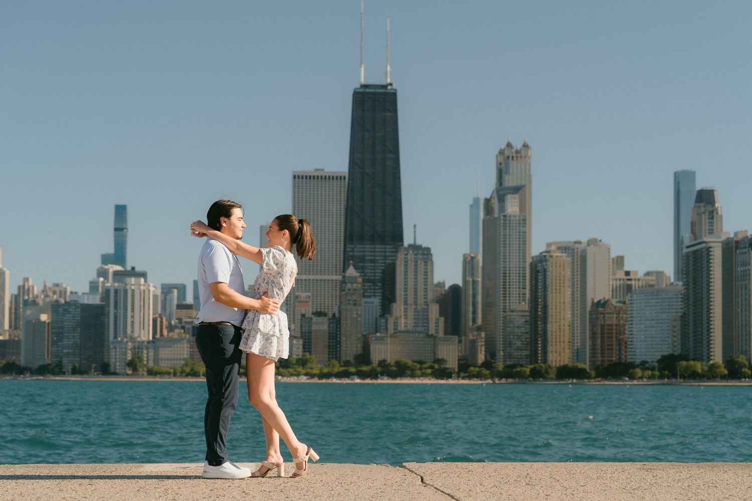 Engaged couple dancing together on Chicago lakefront with iconic city skyline behind them.