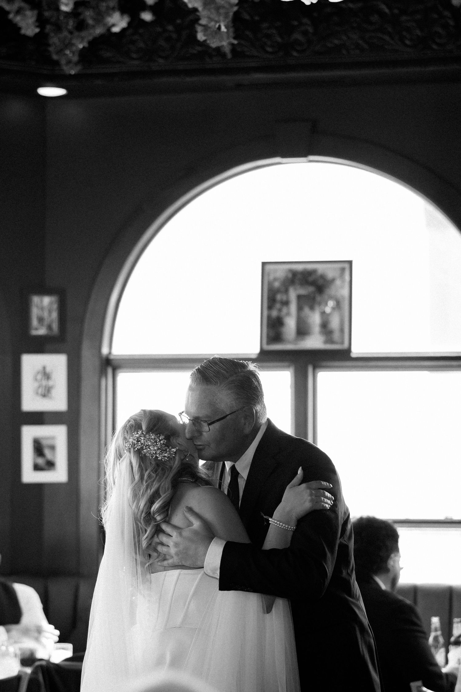 Black and white photo of a bride and her father sharing an emotional first dance embrace at a wedding reception.