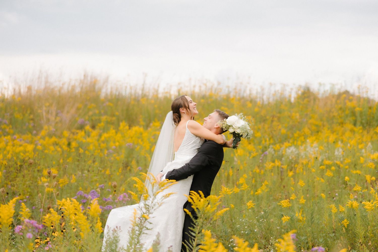 Groom dipping bride in a lush yellow wildflower field during romantic outdoor wedding portraits.