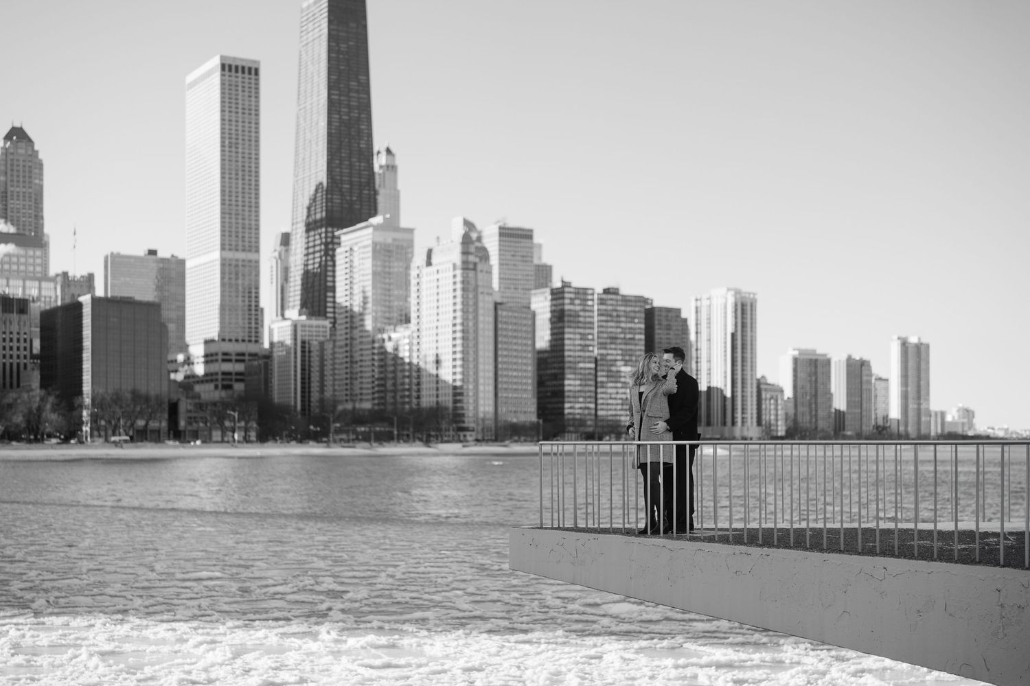 Black and white photo of couple at Chicago lakefront pier with city skyline.