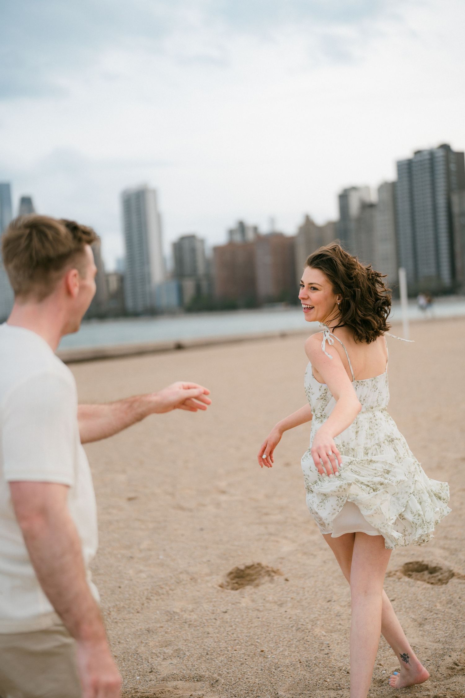 Woman laughing joyfully as couple plays on Chicago beach with city skyline backdrop.