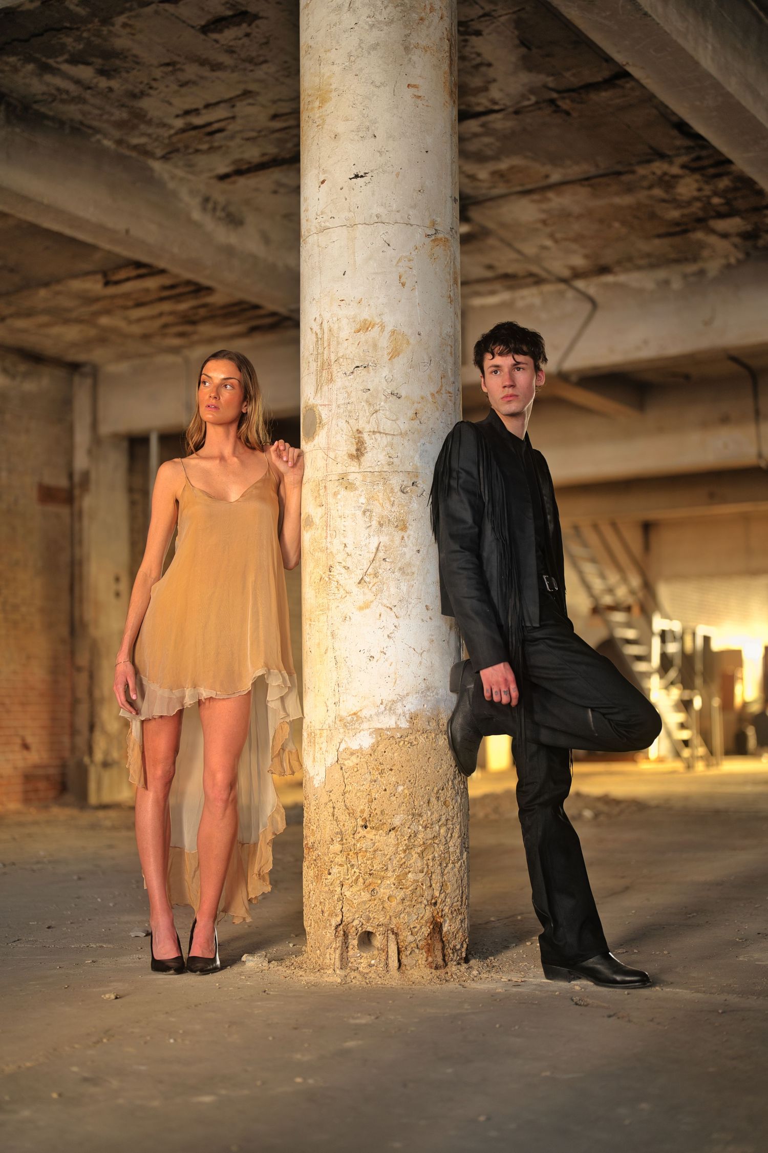 Man and woman leaning on concrete pillar.