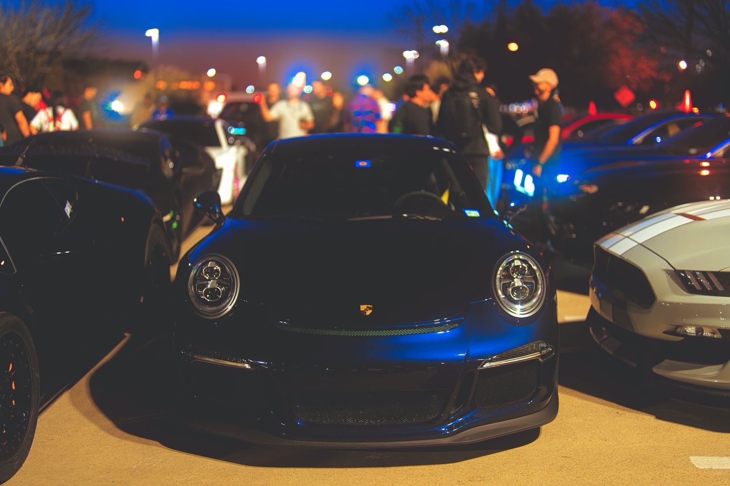 Porsche 911 parked in the sunset with people around.