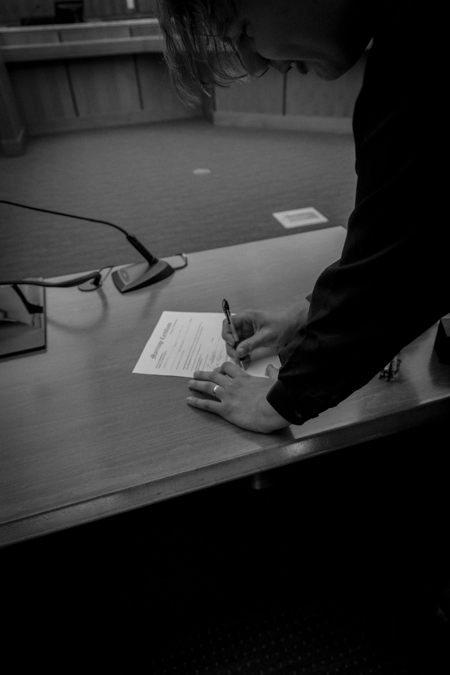 Groom signing wedding documents at courthouse table in black and white photo.