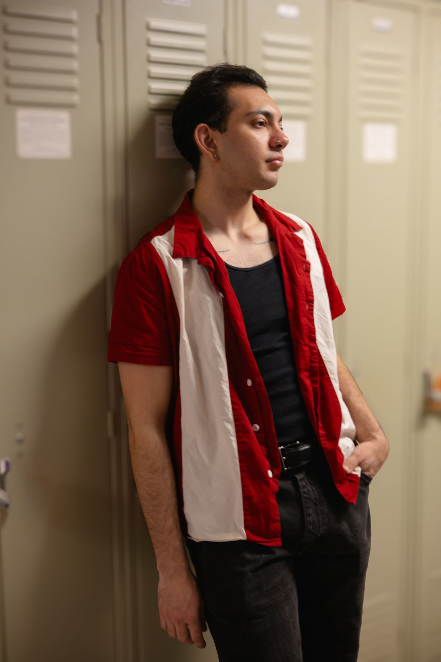 Young man in red and white bowling shirt leaning against school lockers looking away.
