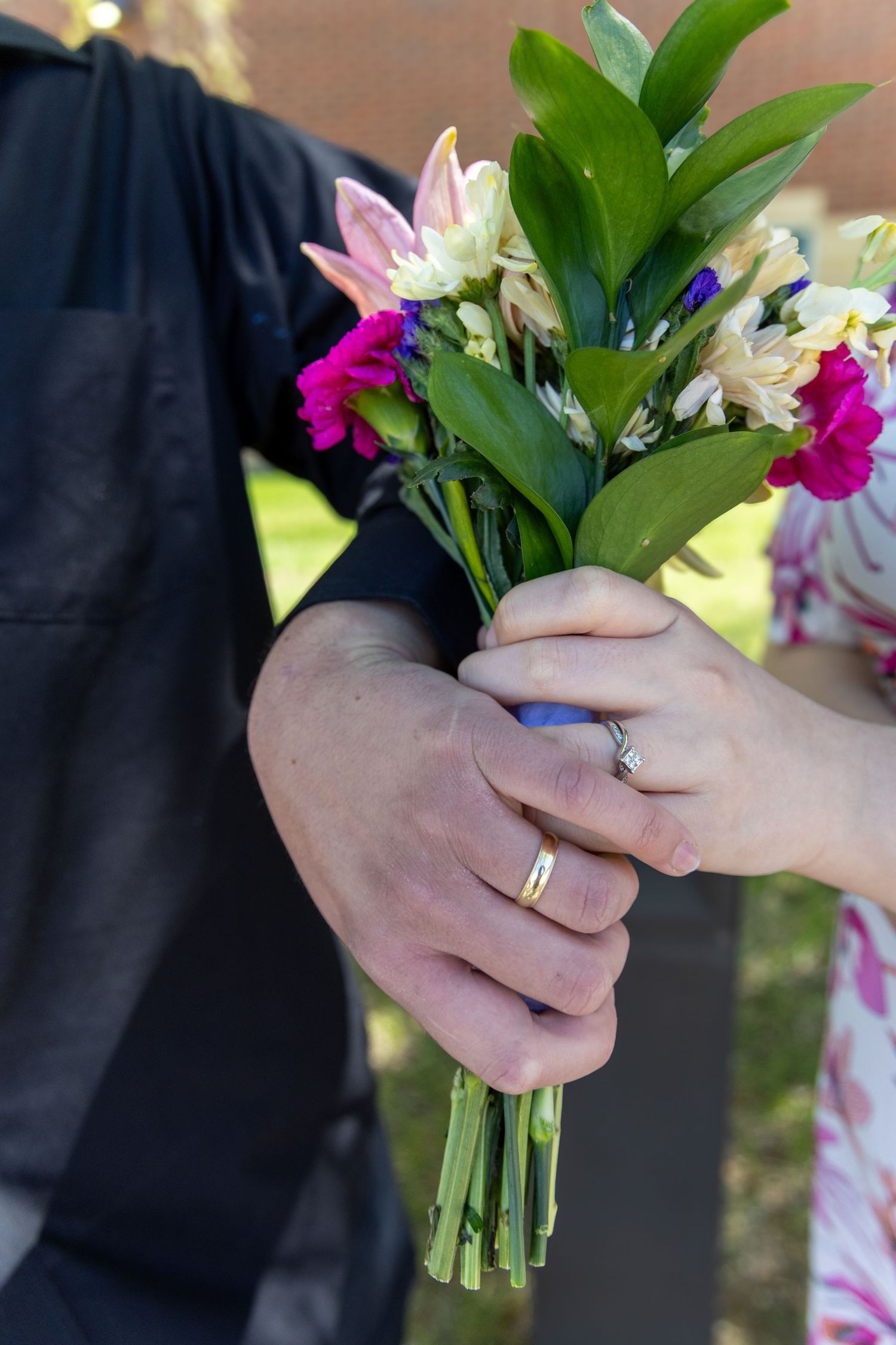Newlywed couple holding colorful bridal bouquet with wedding rings visible.
