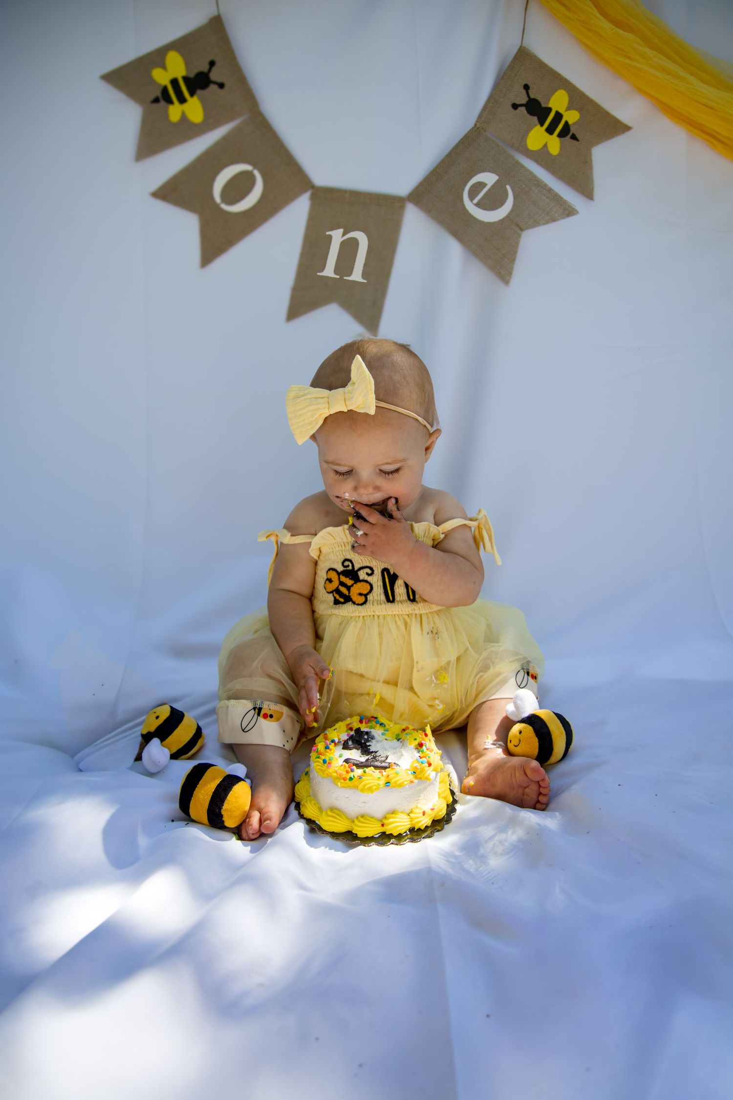 Baby girl in yellow tutu eating cake at a bee-themed first birthday party with \