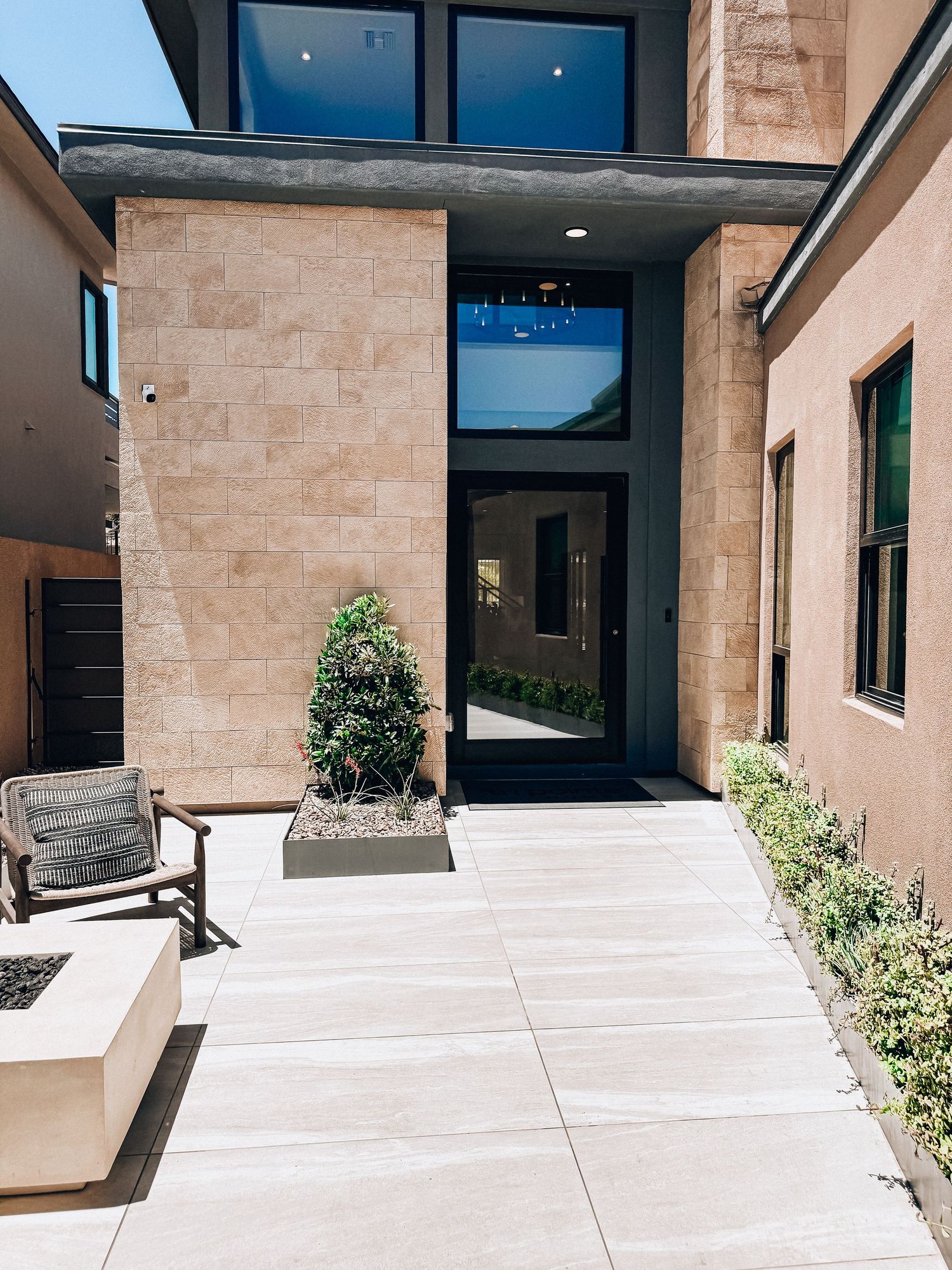 Modern home entrance with stone facade, large glass door, and concrete patio in a contemporary architectural design.