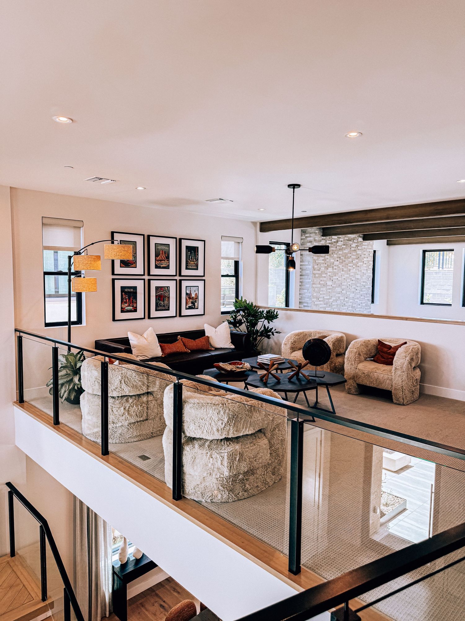 Modern open-plan living room with glass railing balcony, gallery wall, plush sofas, and pendant lighting in a luxury home.