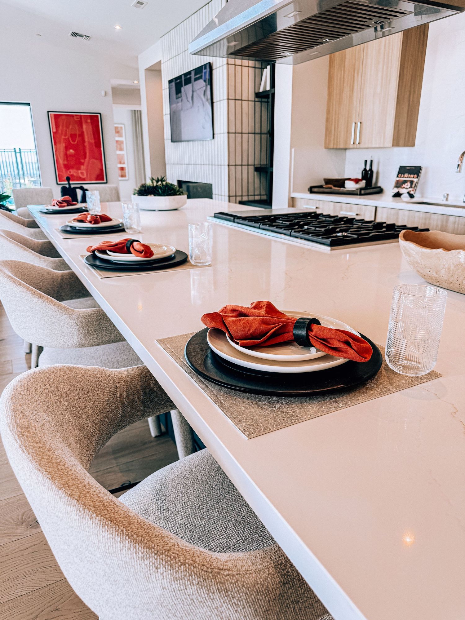 Modern kitchen island with white countertop, black plates, red napkins, and beige barrel chairs in a stylish open-plan kitchen.