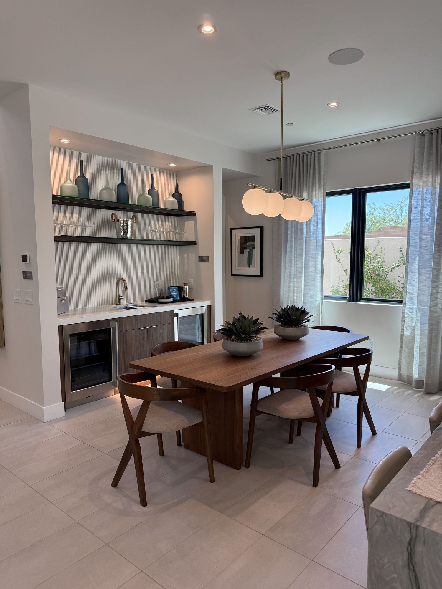 Modern dining room with walnut table, mid-century chairs, built-in wet bar, open shelving, and pendant lighting in a bright white space.