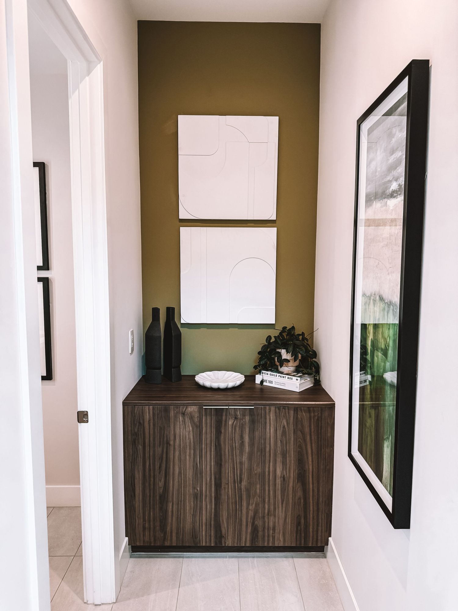 Modern hallway nook with walnut cabinet, white textured wall art, black vases, and olive green accent wall.