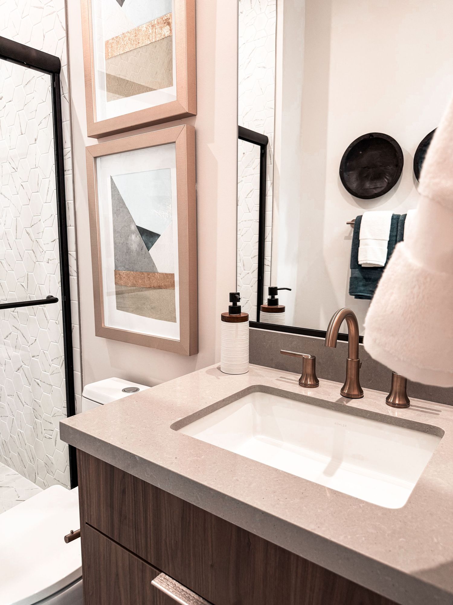 Modern bathroom vanity with bronze faucet, quartz countertop, framed artwork, and large mirror above undermount sink.