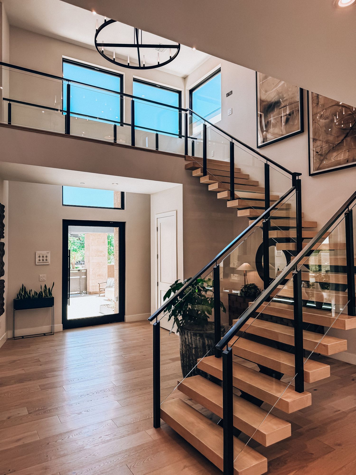 Modern home entryway with floating wood staircase, black metal railings, hardwood floors, and soaring two-story windows.