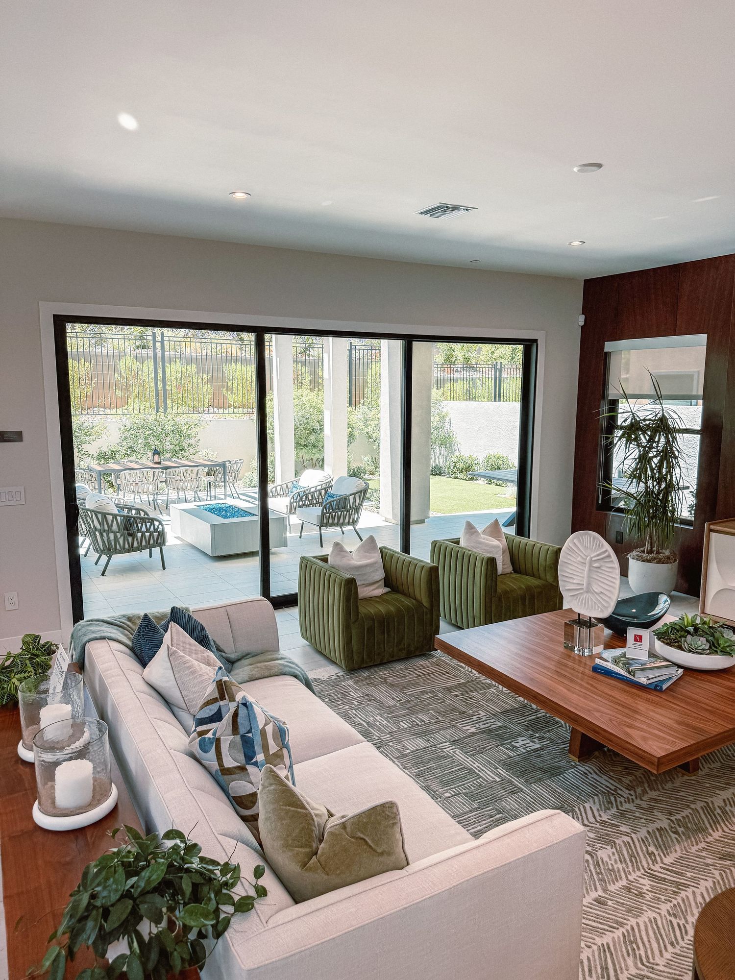 Modern open-plan living room with large sliding glass doors, green armchairs, white sectional sofa, and view of outdoor patio.