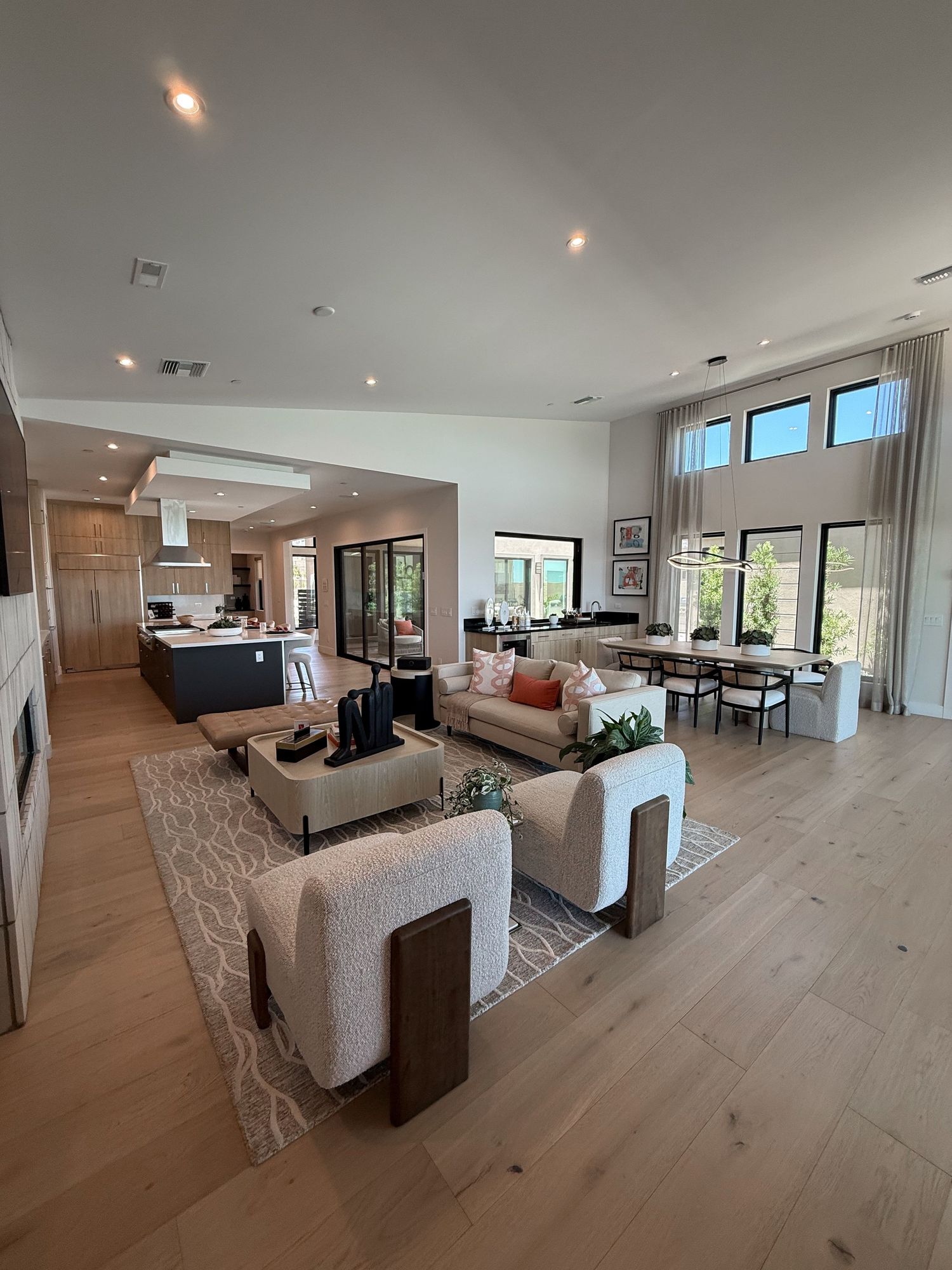 Spacious open-concept living room with light hardwood floors, neutral sofas, and modern kitchen in background.