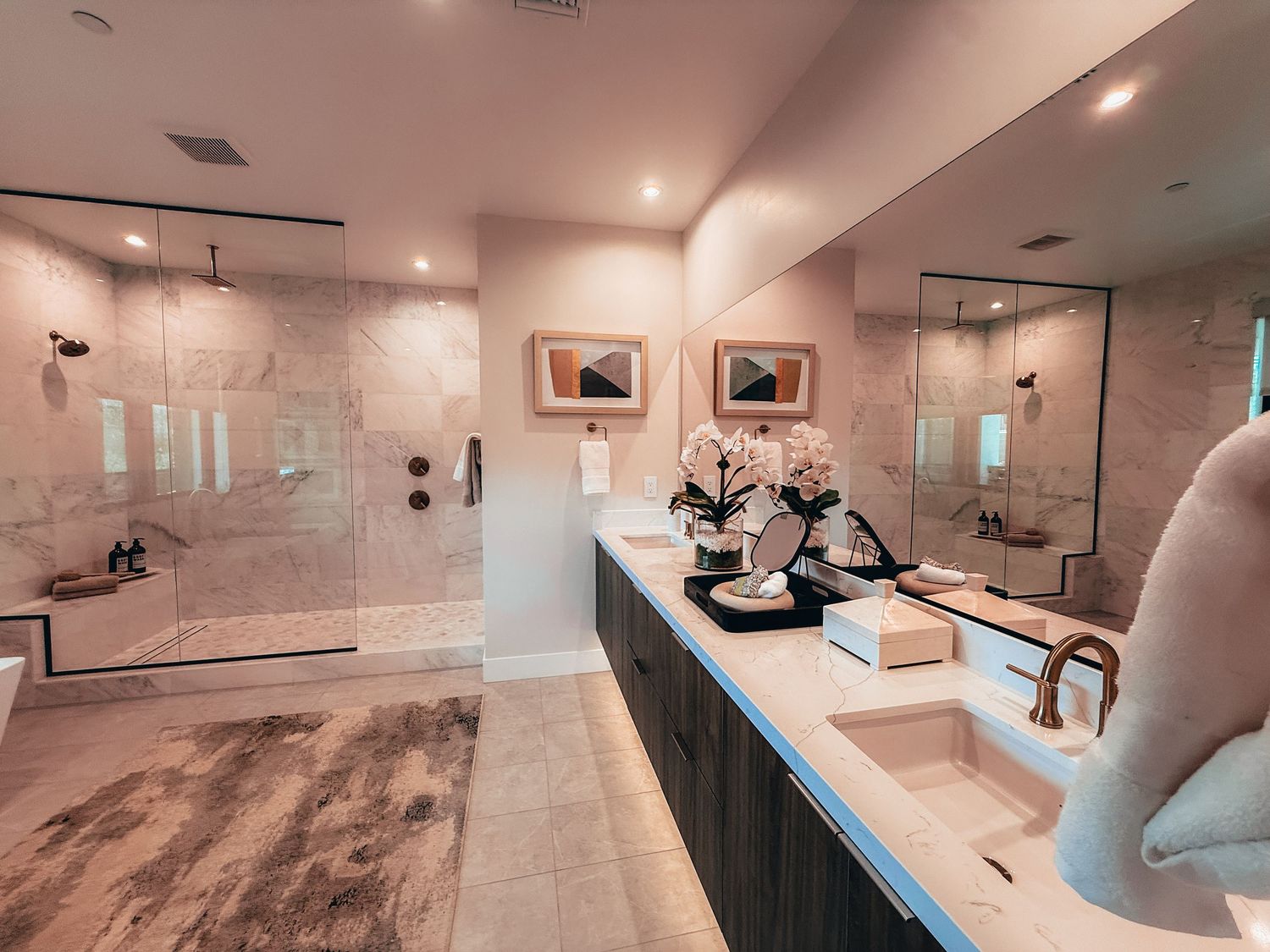 Luxurious master bathroom with marble walls, glass shower, soaking tub, dual vanity sinks, and elegant floral decor.