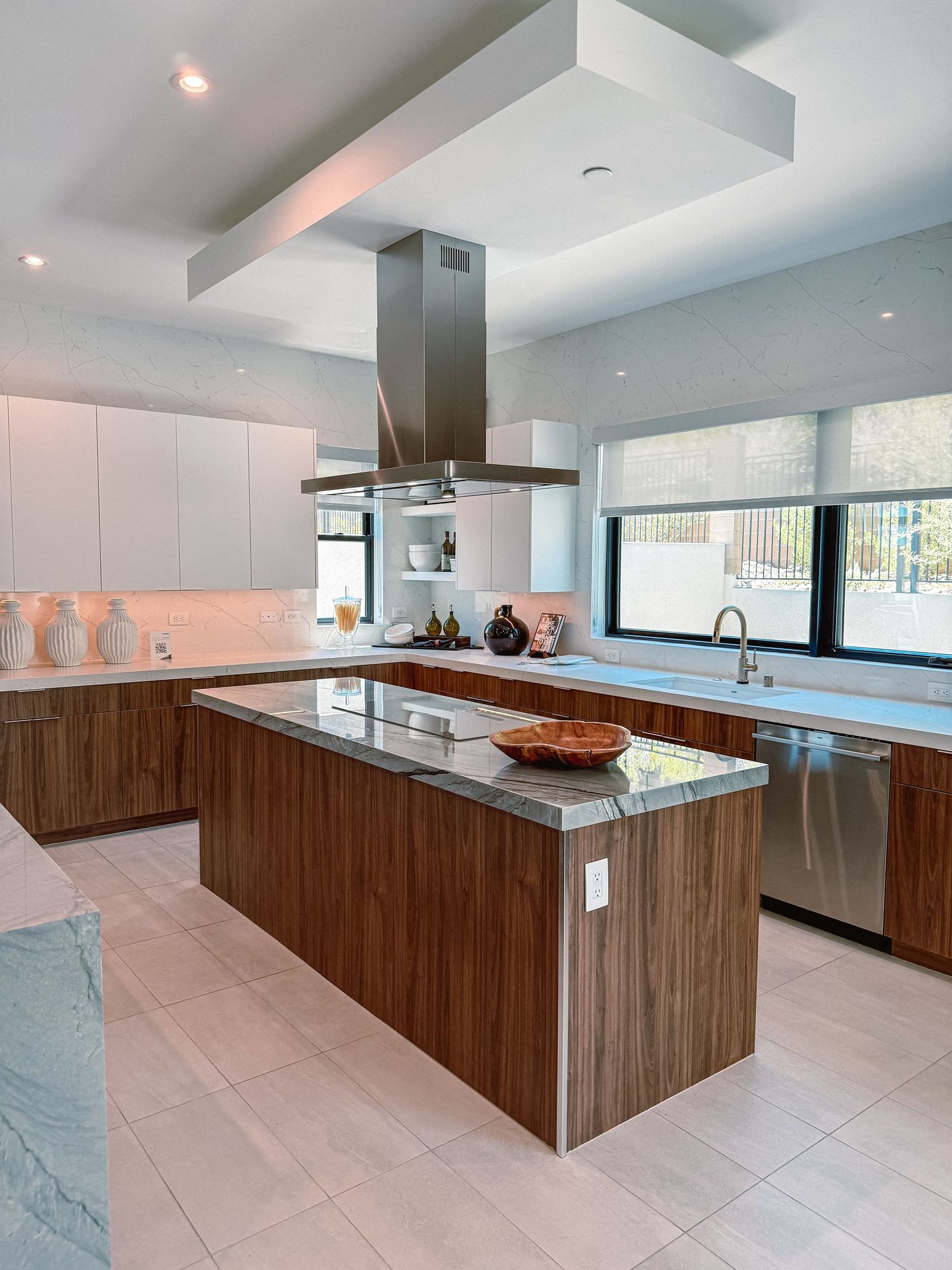 Modern kitchen with wood grain island, stainless steel range hood, white cabinets, and large windows.
