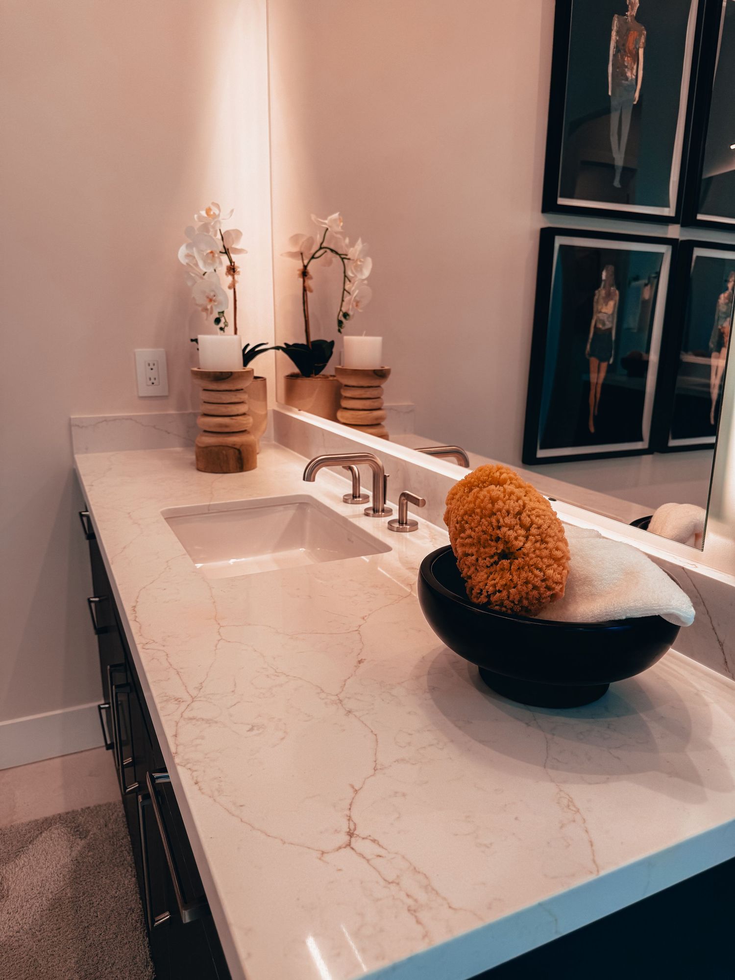 Elegant marble bathroom vanity with undermount sink, orchid decor, wooden accents, and framed fashion artwork on pink walls.